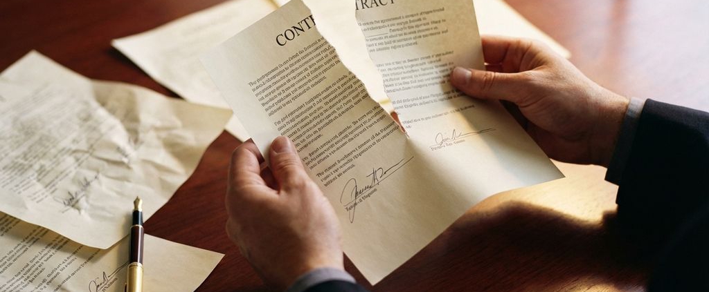 Zakenhand houdt verscheurd contract vast op mahoniehout bureau met verspreid papier en gouden vulpen