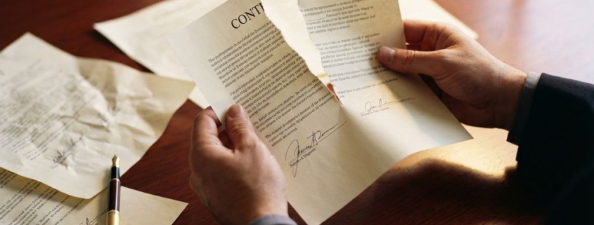 Zakenhand houdt verscheurd contract vast op mahoniehout bureau met verspreid papier en gouden vulpen