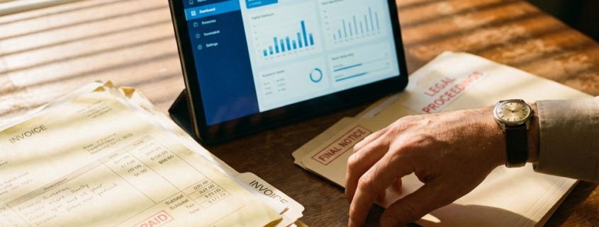 Zakenman reikt naar juridische documenten op houten bureau met onbetaalde rekeningen en tablet met incassobureau-interface