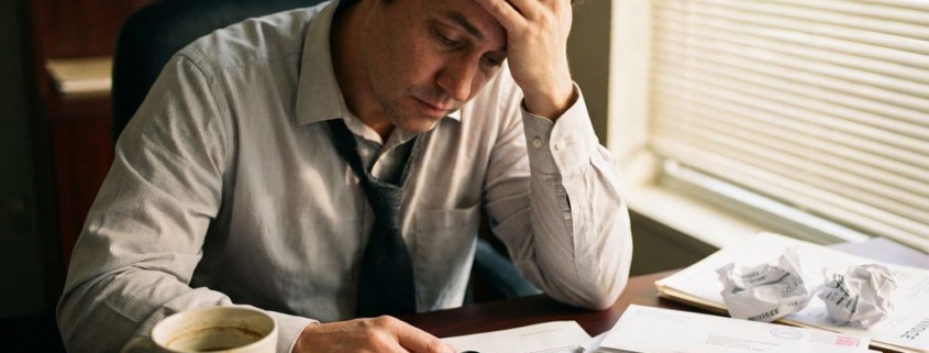 Gefrustreerde zakenman aan bureau met onbetaalde facturen, ongeopende envelop en smartphone met gemiste oproepen