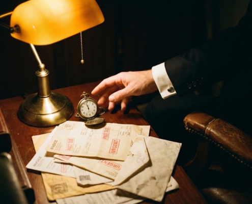 Zakenman reikt naar vintage zakhorloge op bureau met onbetaalde facturen, klok wijst bijna middernacht aan