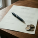 Gedrukt contract op donker eikenhouten bureau met zwarte pen en euromunten in natuurlijk licht.