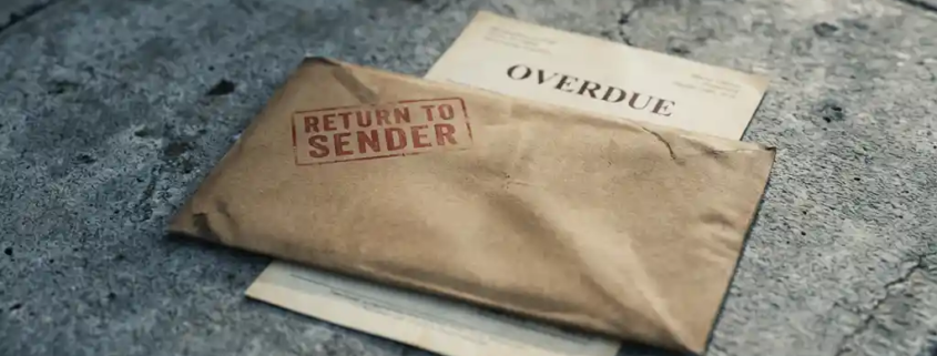 Bruin envelop met rood "return to sender"-stempel op betonnen ondergrond, gedeeltelijk zichtbare achterstallige factuur eronder.