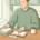 Ondernemer aan houten bureau met georganiseerde facturen, openstaand kasboek en kop koffie in zacht daglicht.