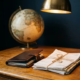 Opengeslagen leren paspoort op een eikenhouten bureau naast internationale facturen, met een vintage globe en een messing bureaulamp op de achtergrond.