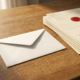 Verzegelde witte envelop op een eiken bureau naast een stapel papieren facturen met een rood stempel, warm middagslicht.
