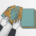 Hand organiseert stapel onbetaalde facturen op kantoorbureau, bovenaanzicht in teal en amber tinten.